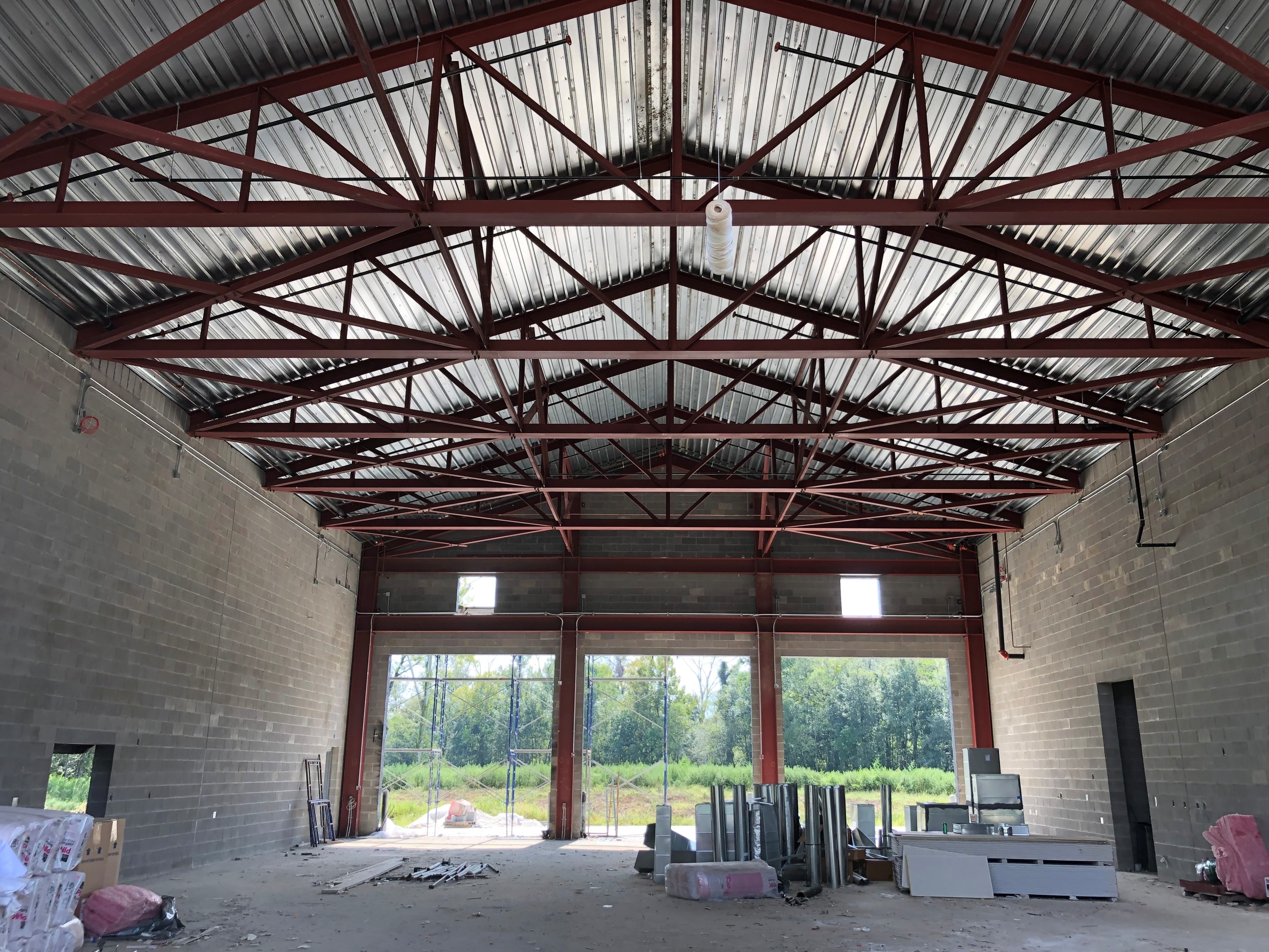 Fire Station 20 engine bay interior showing red structural steel trusses and corrugated metal roof decking under construction