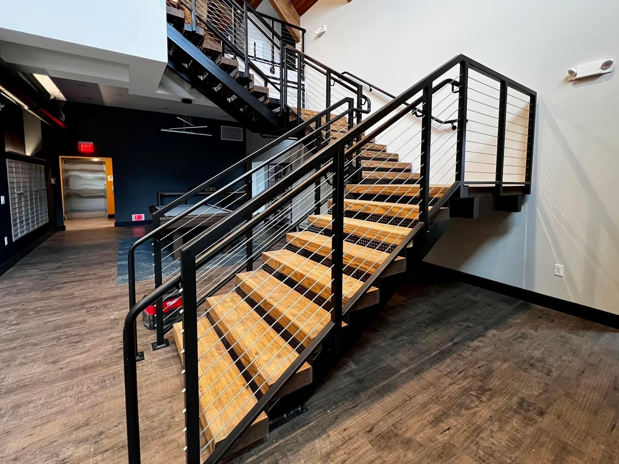 The Clubhouse entry staircase close-up showing wood treads, black metal stringers, and stainless cable railings