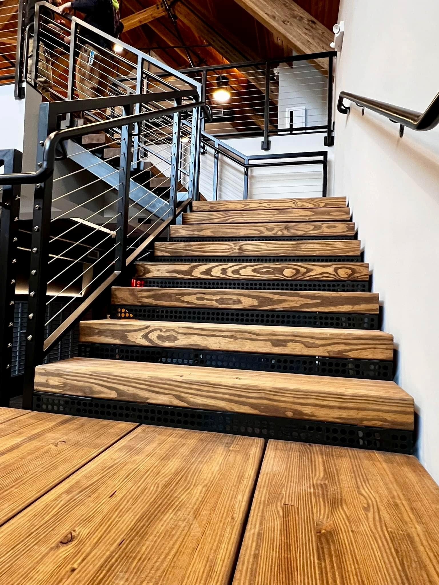 The Clubhouse staircase looking up showing wood grain treads and perforated metal risers under timber ceiling